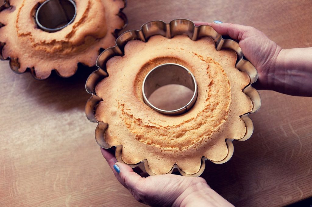 A freshly baked cake in a fluted mold held in hands over a kitchen table.
