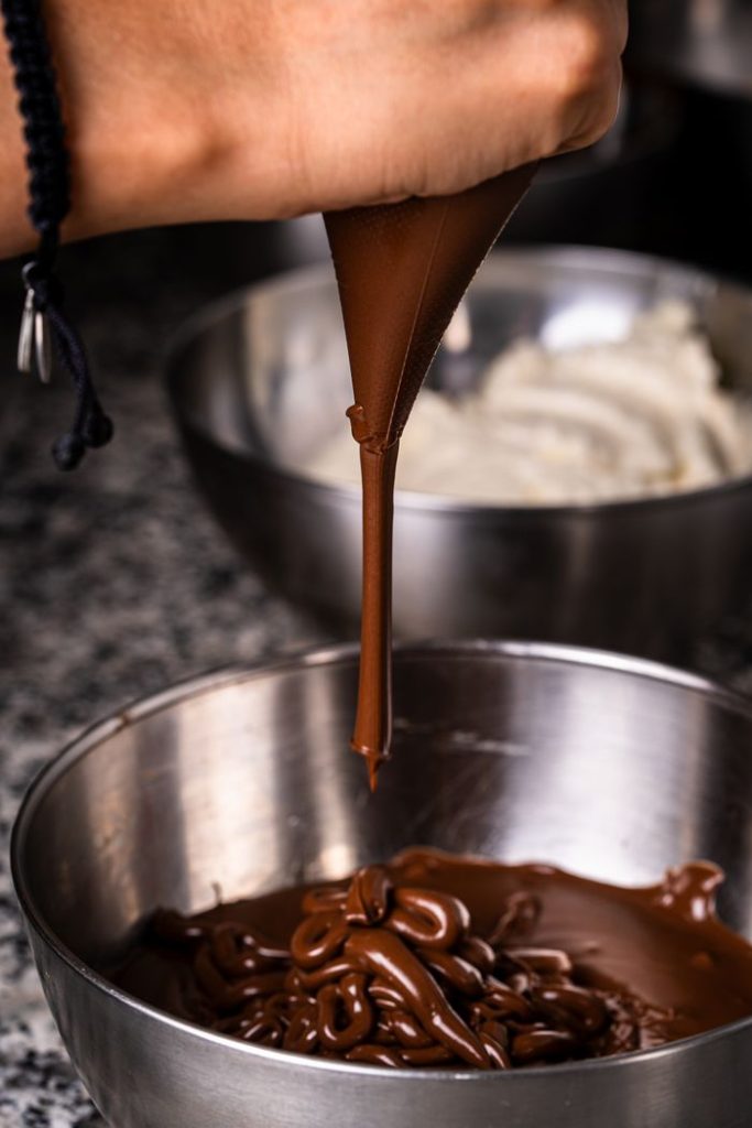 Hand pouring rich melted chocolate into a mixing bowl, perfect for baking enthusiasts.